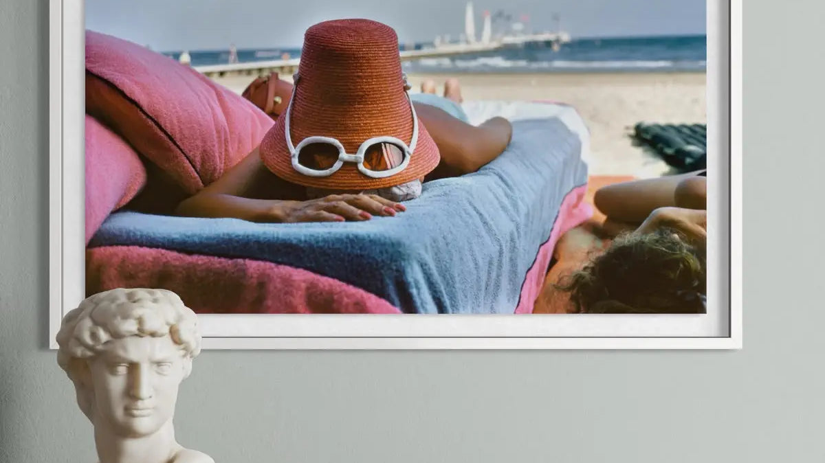 A Vintage beach photograph by Slim Aarons of a woman tanning with a hat and a pair of white glasses