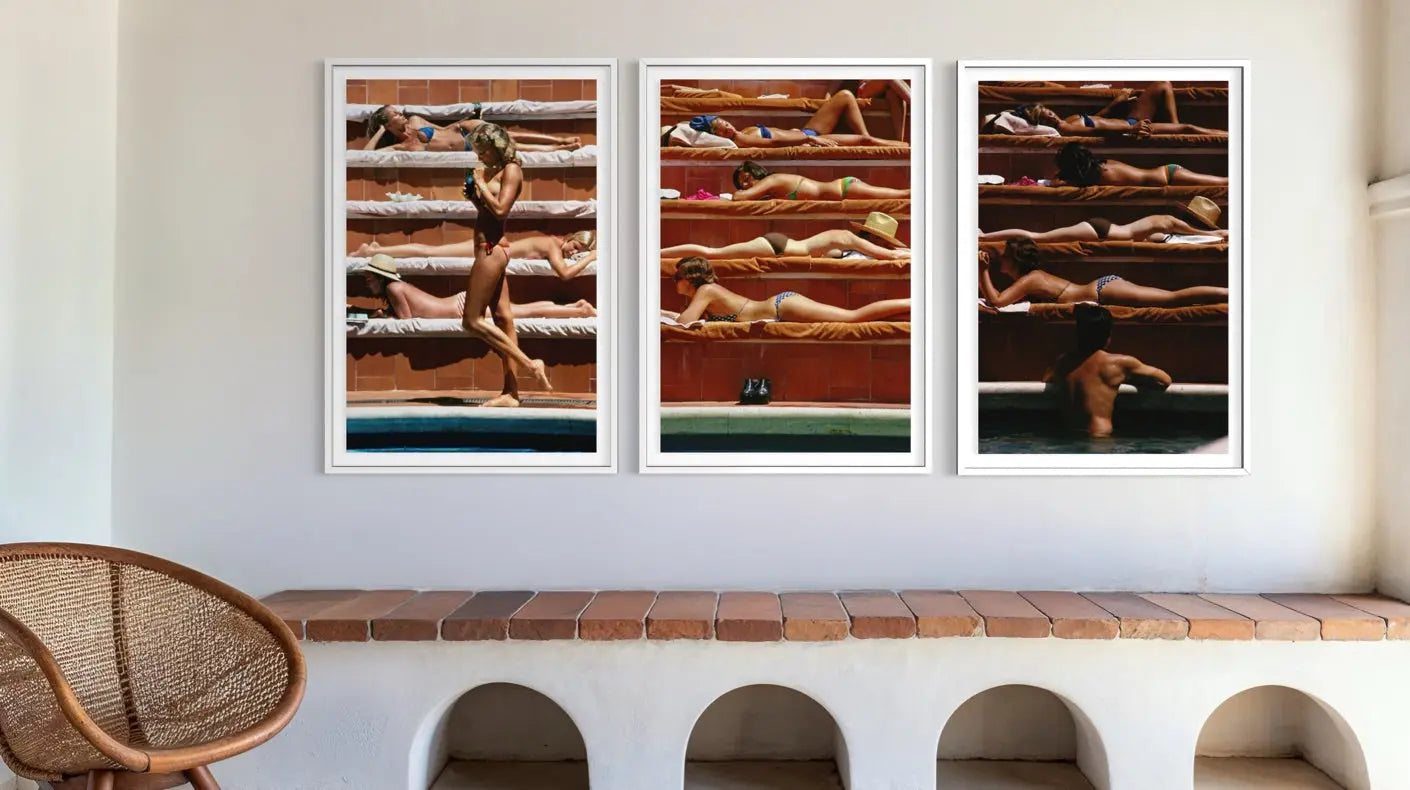 A set of three framed vertical photographic prints depicting sunbathers in a pool area, displayed on a white wall above a terracotta bench in a modern interior setting.