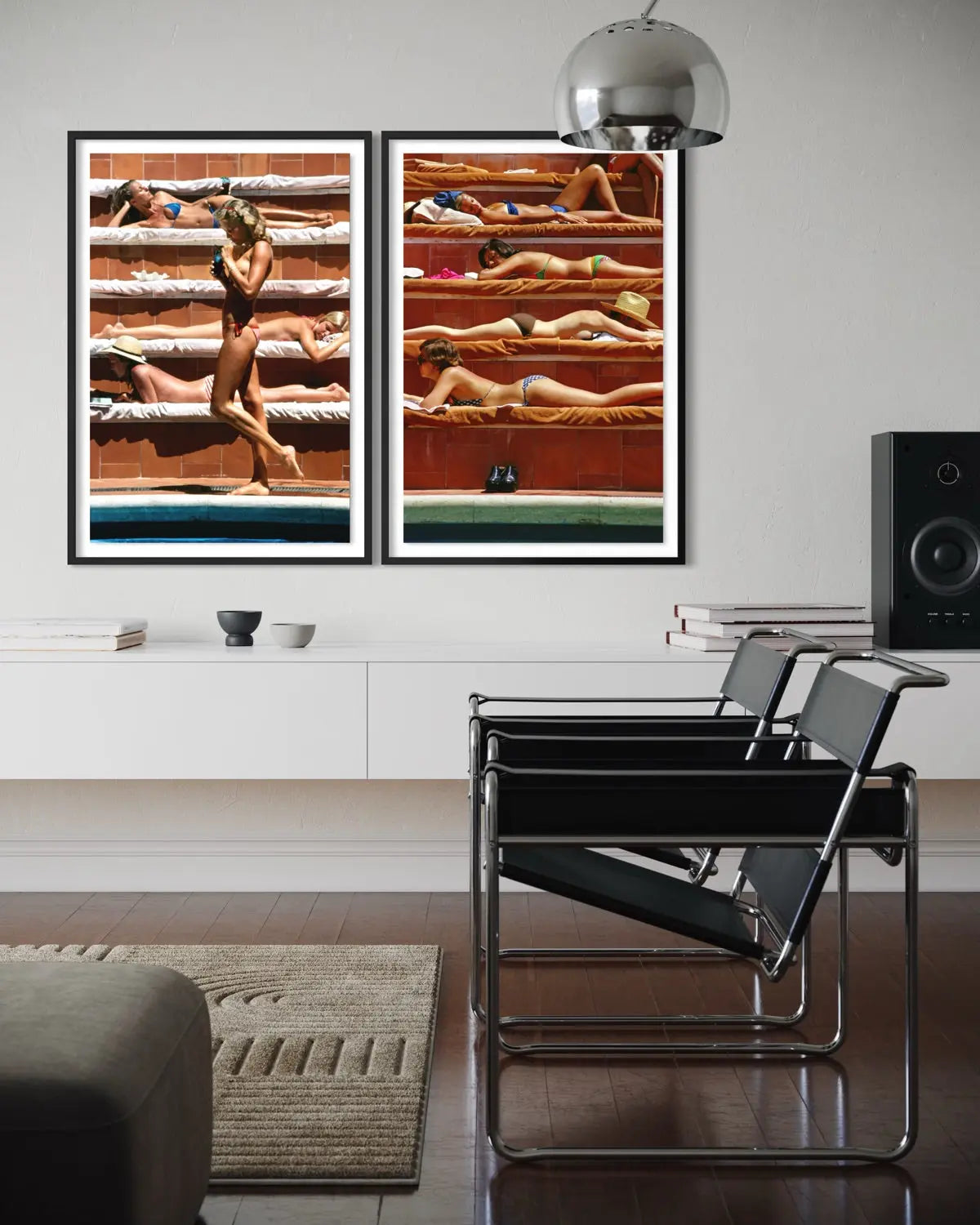 A modern interior room scene showing two vertical framed art prints hanging on a white wall above a console. The prints depict sunbathing figures on wooden benches in warm beach-like tones.