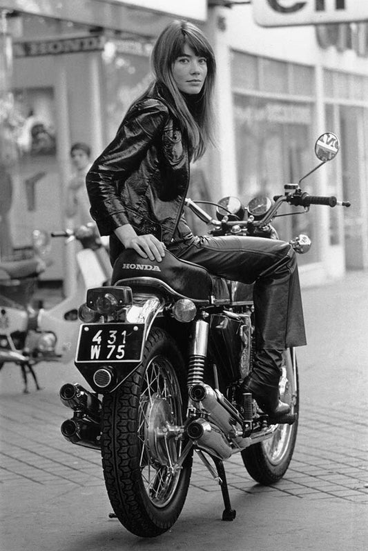 A black and white photograph of Francoise Hardy sitting on a Honda CB750 motorcycle, taken by Reg Lancaster.