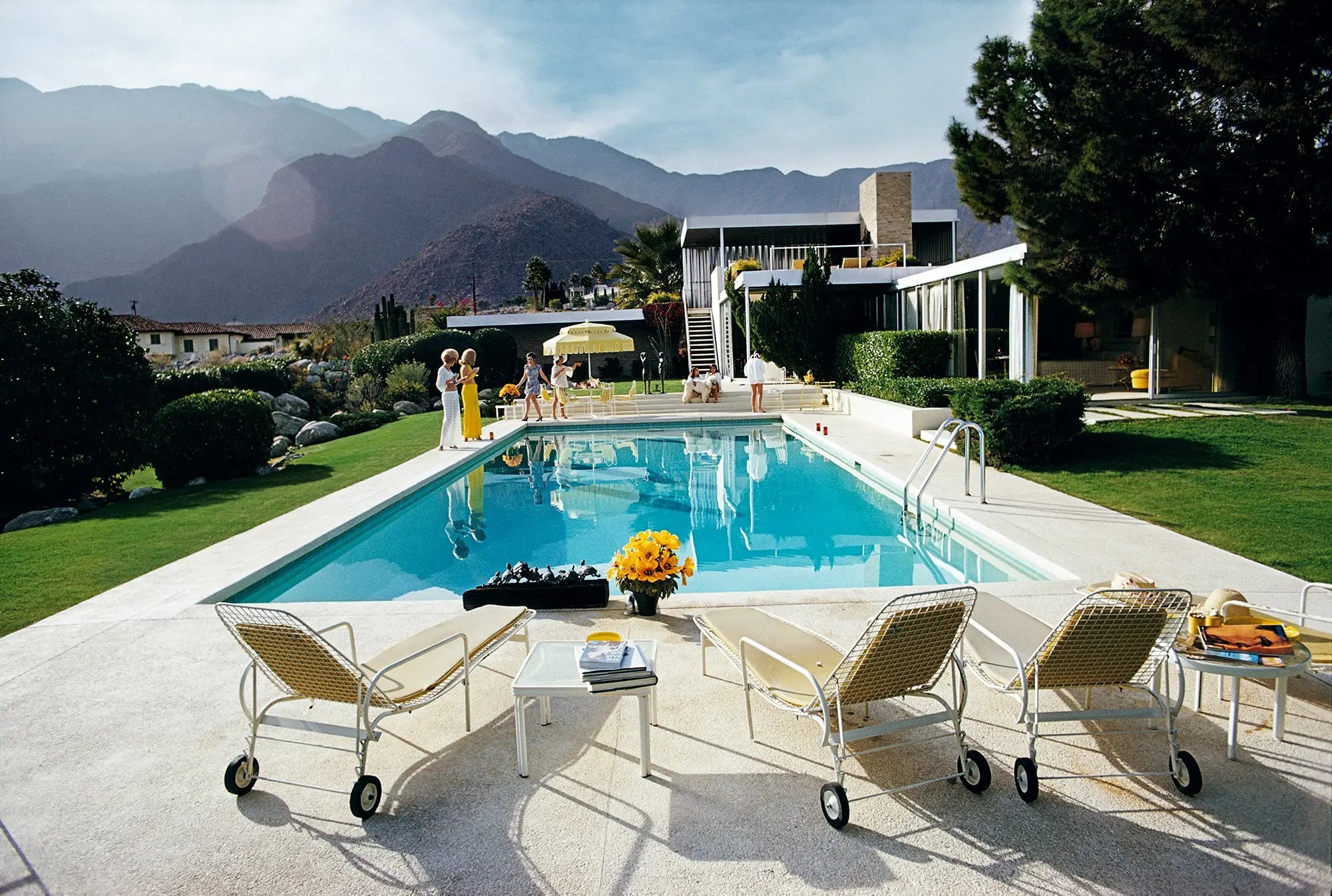 Pool area with lounge chairs, table, and flowers with mountains in the background. The Picturalist Wall Art and Photography for Designed Interiors. Slim Aarons Collection, Poolside. Getty Images Gallery.