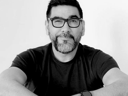 Black and white photo of a man with glasses and a beard wearing a black t-shirt.