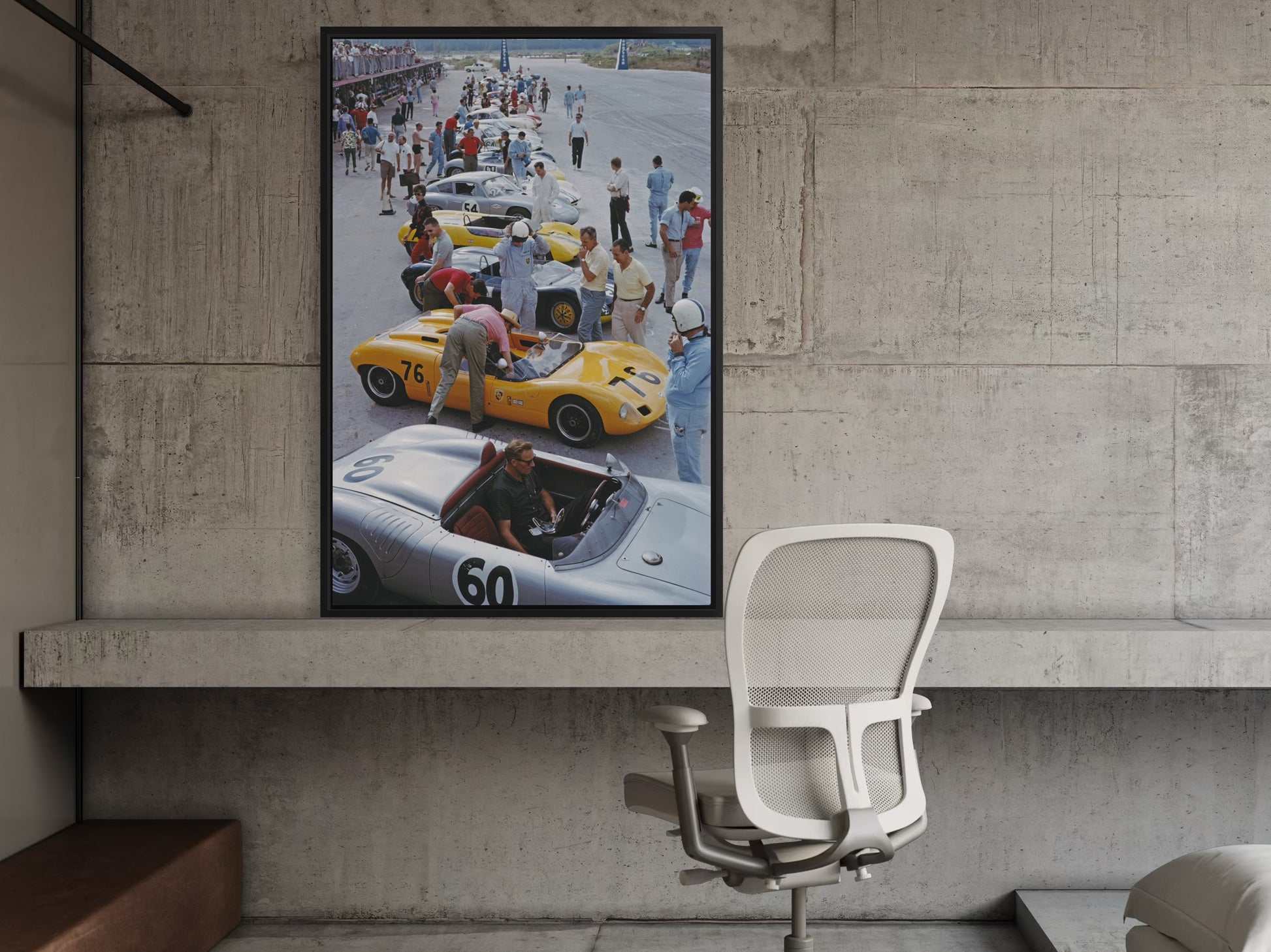Framed poster of a race car scene on a concrete wall above a chair.