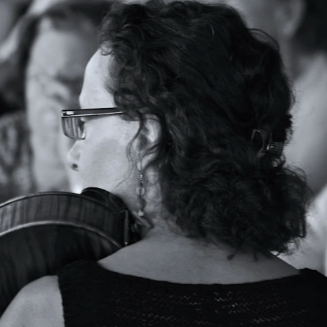 Person with glasses and dark hair, wearing a black top, sitting in an auditorium.