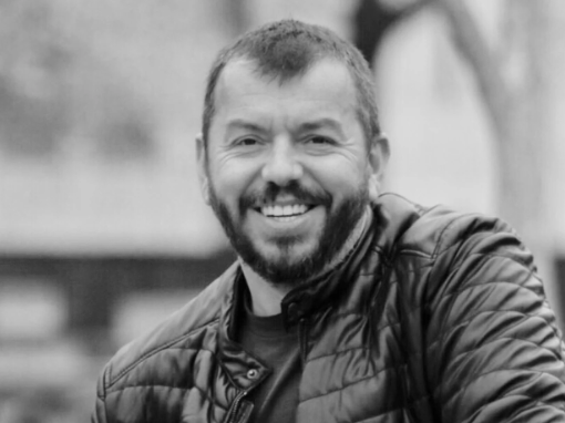 Black and white photo of a man with a beard smiling outdoors