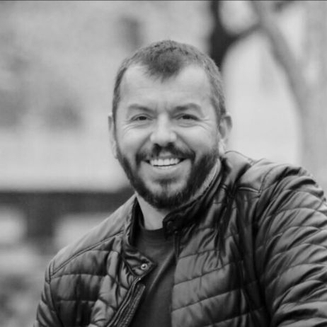 Black and white photo of a man with a beard smiling outdoors
