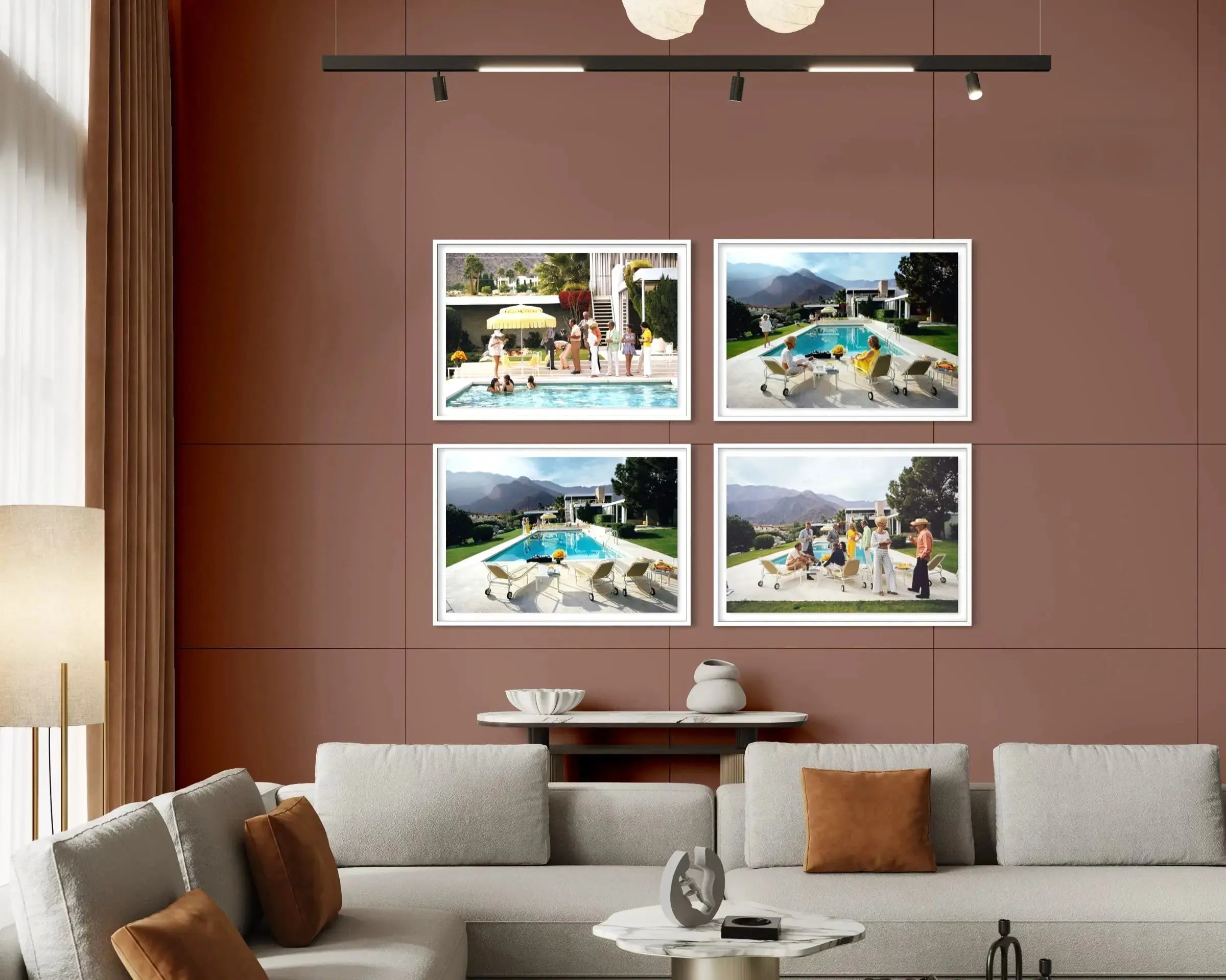 A modern living room setting featuring a wall-mounted four-panel framed print set. The prints showcase scenic poolside and mountain views, styled on a terracotta-colored wall above a light gray sectional sofa. The Picturalist Wall Art and Photography for Designed Interiors. Slim Aarons Collection, Poolside. Getty Images Gallery.