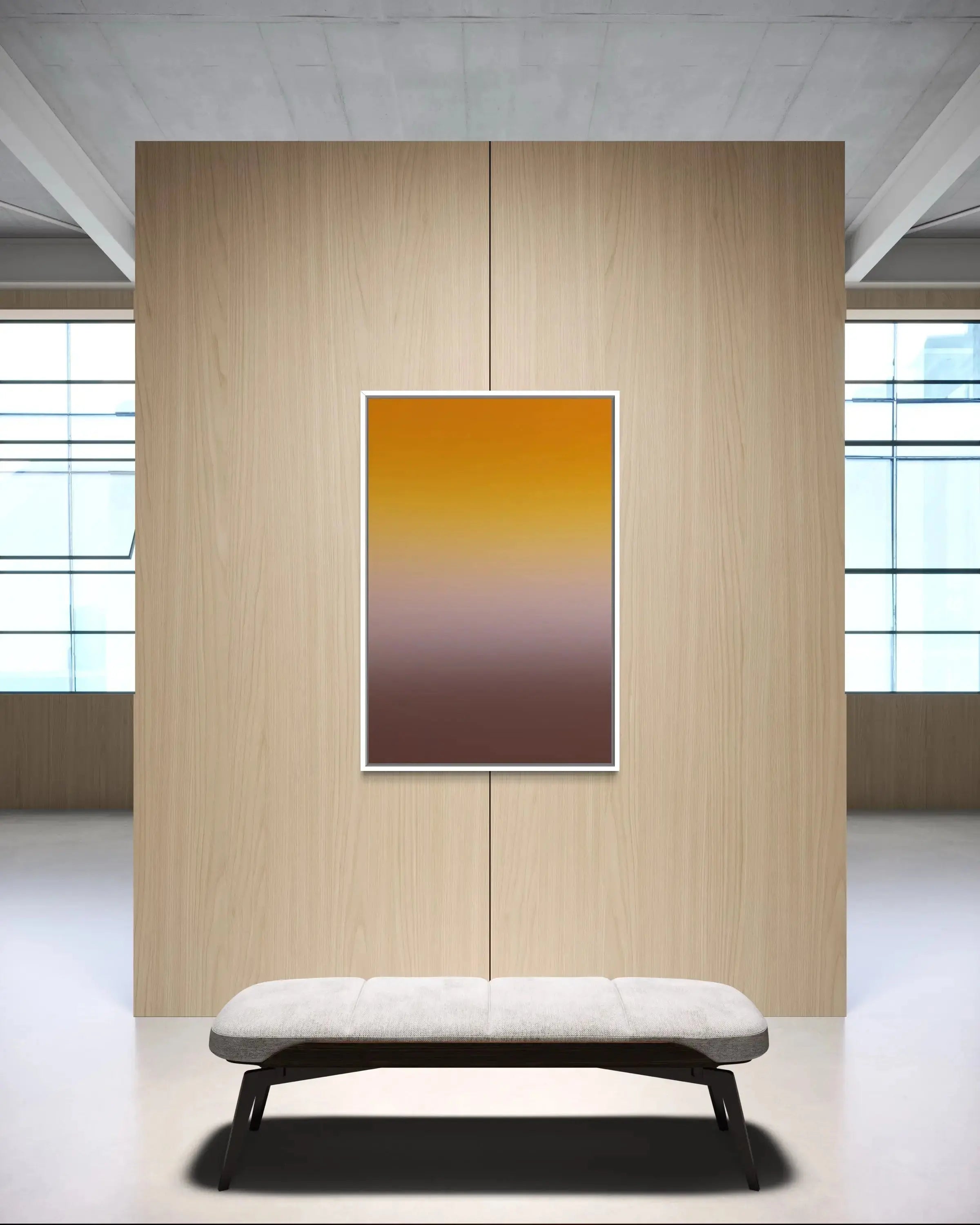 A vertical framed art print featuring a smooth yellow-to-brown gradient, displayed on a light wood panel wall above a modern white bench in a minimalist interior setting.