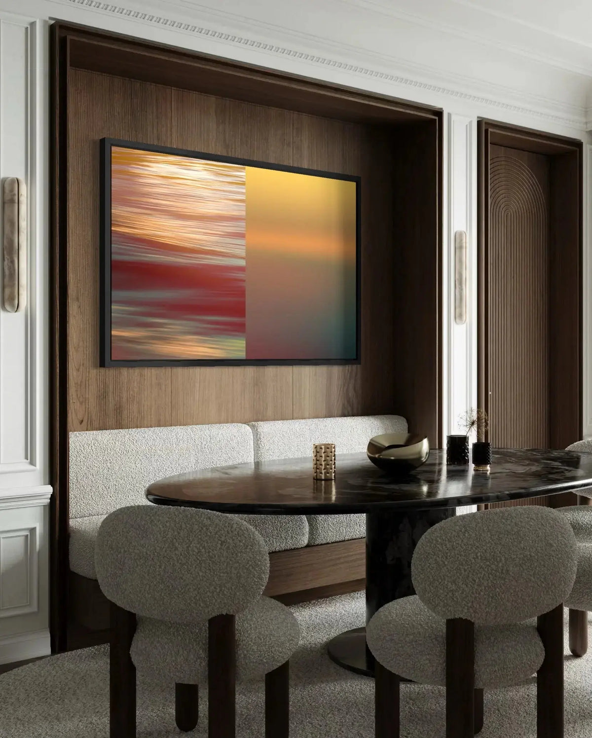 A framed abstract wall art print with a split red-orange and yellow design hangs on a dark wood-paneled wall above a dining area with upholstered chairs and a dark table.