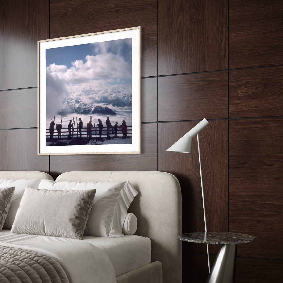 A framed art print depicting a scenic mountain landscape with silhouetted figures under a cloudy sky, styled on a dark wood-paneled wall above a bed in a modern bedroom setting.