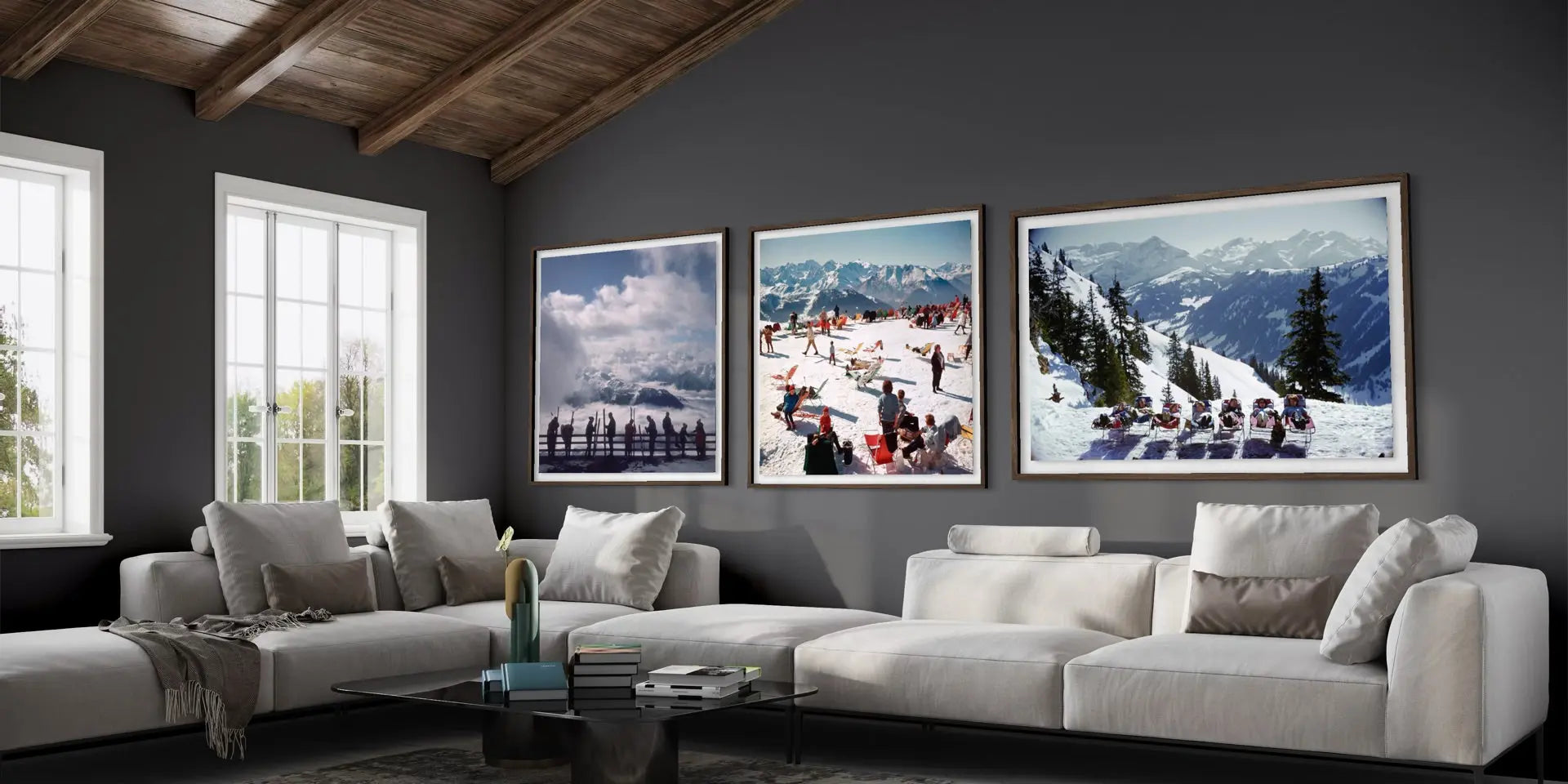 Three framed winter mountain art prints displayed on a dark gray wall above a modern white sectional sofa in a styled living room.
