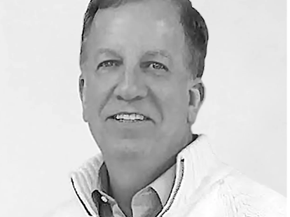 Black and white photo of a man wearing a white sweater with a logo on a light gray background