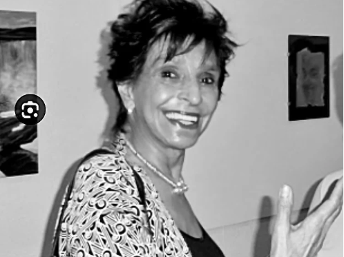 Black and white photo of a woman smiling indoors with decorative elements on the wall.