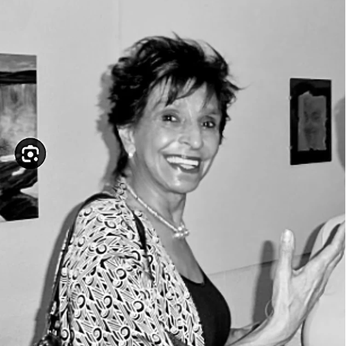 Black and white photo of a woman smiling indoors with decorative elements on the wall.