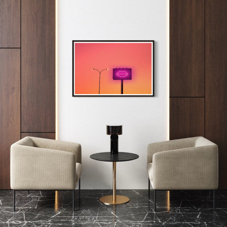 Modern interior with two beige armchairs, a small black table, and a vibrant pink and orange framed artwork on a white wall.