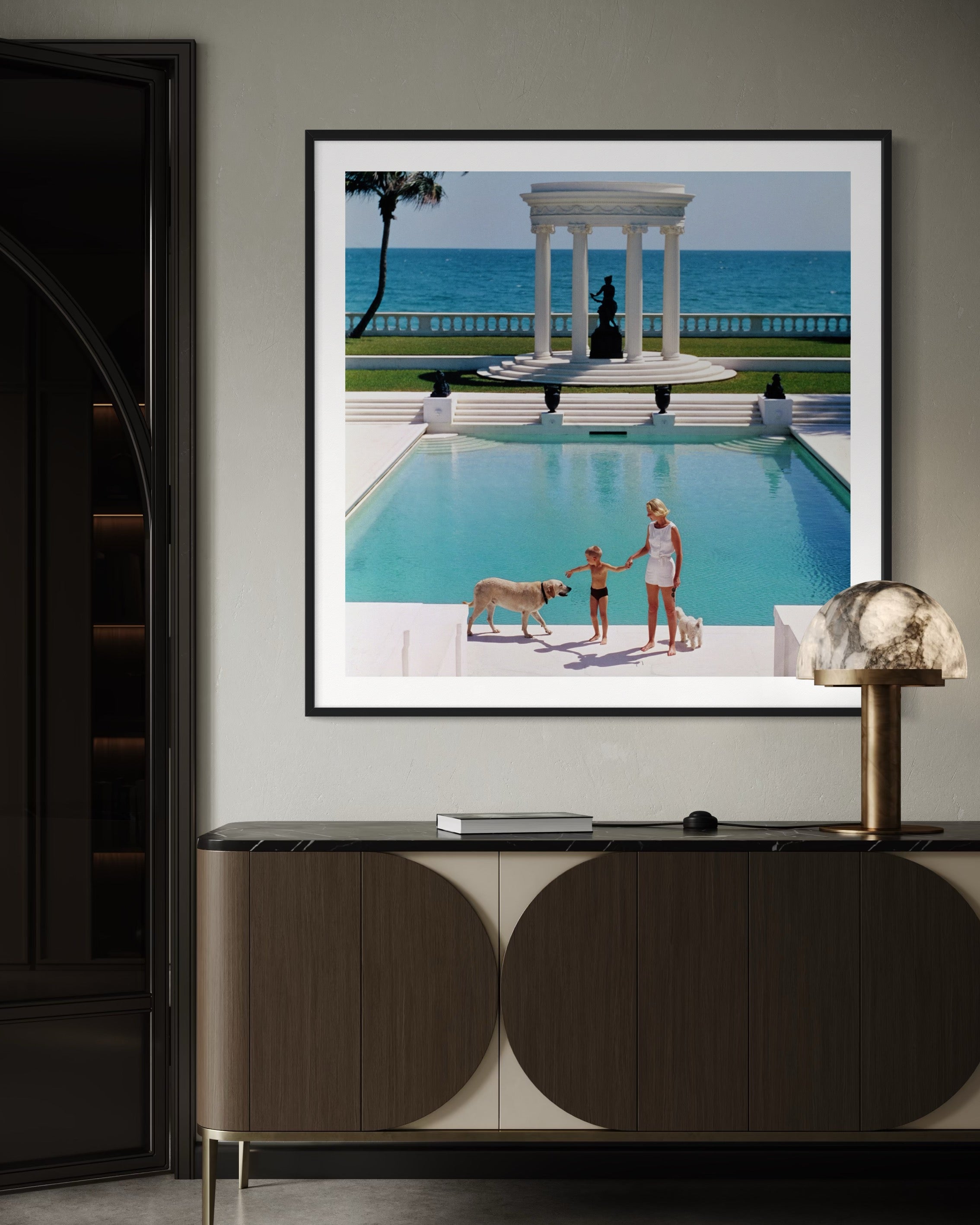 Framed photograph of a pool scene with people and a dog, displayed on a wall above a cabinet.