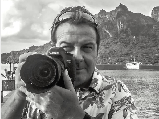 Person holding a Canon camera with a scenic background of mountains and water.
