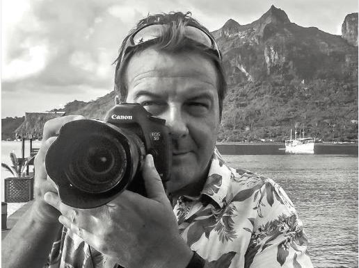 Person holding a Canon camera with a scenic background of mountains and water.