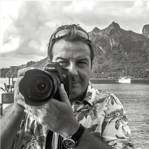 Person holding a Canon camera with a scenic background of mountains and water.
