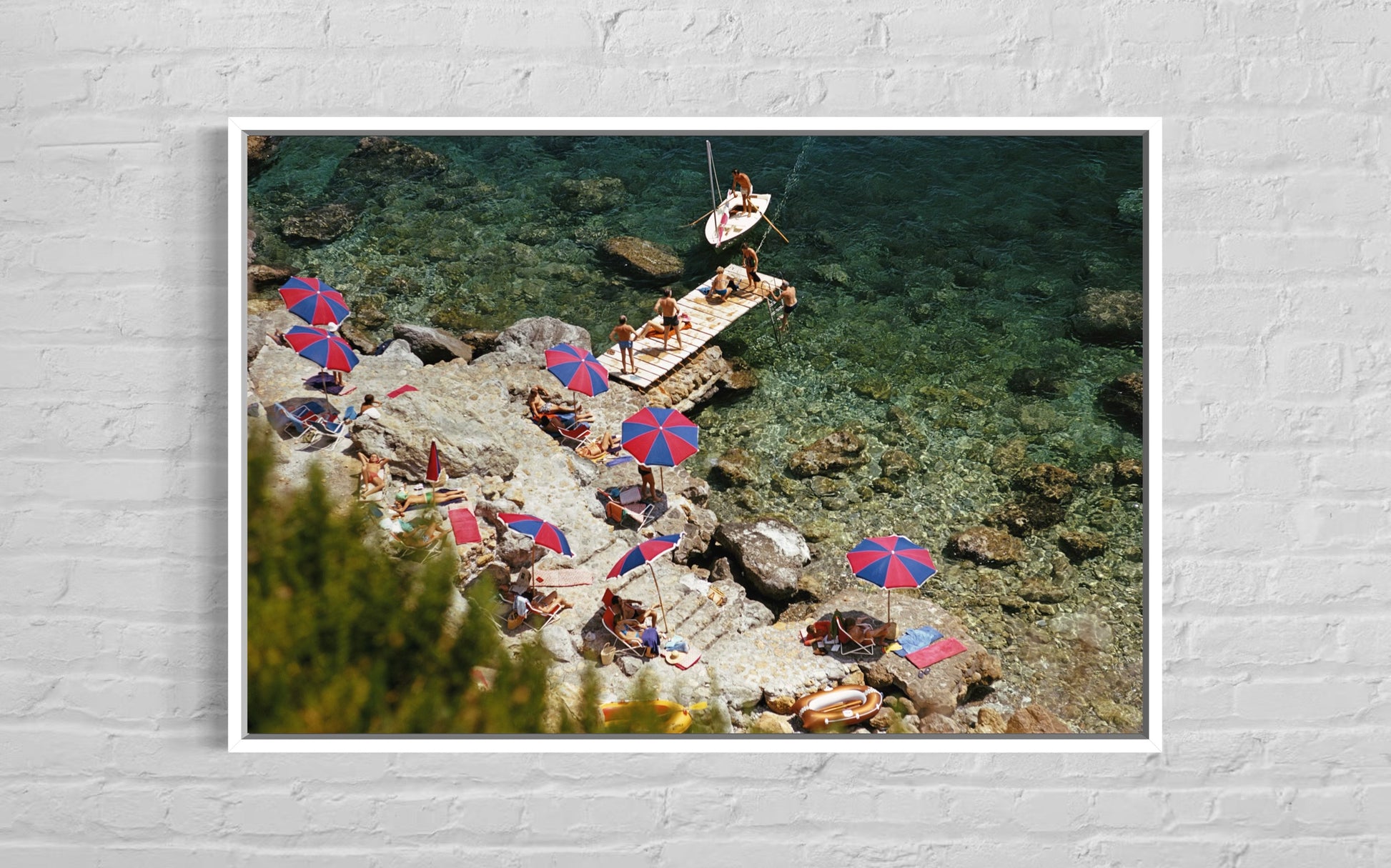 People sunbathing on rocks with colorful umbrellas near a body of water.