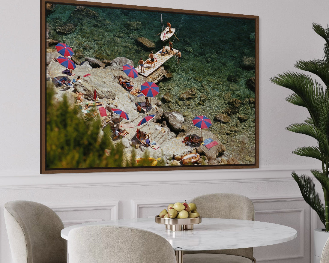 Framed artwork of a beach scene with people and umbrellas above a dining table.