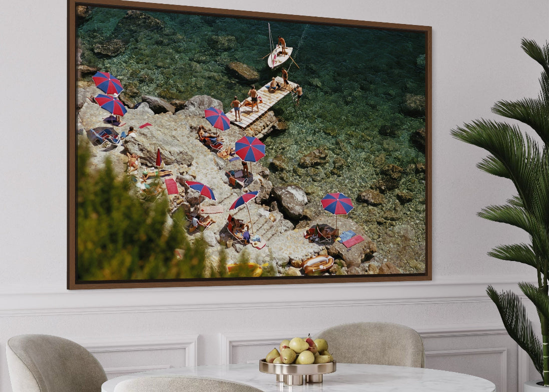 Framed artwork of a beach scene with people and umbrellas above a dining table.
