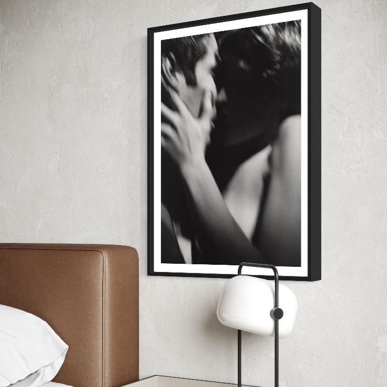 Framed black and white artwork above a bed with a nightstand and lamp.