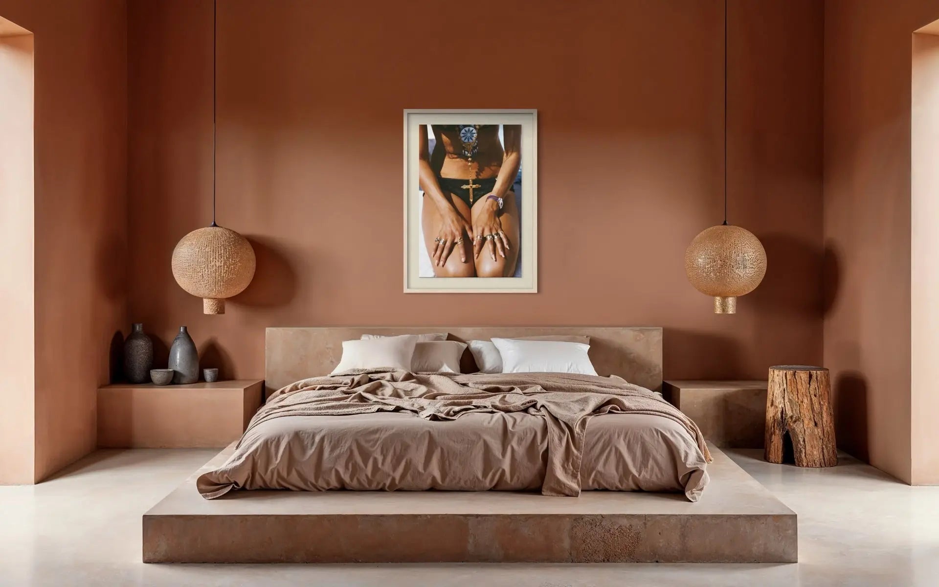 A modern bedroom with a low platform bed, brown bedding, and a terracotta-colored wall featuring a framed art print of a person's torso. Two spherical pendant lights hang on either side of the bed.