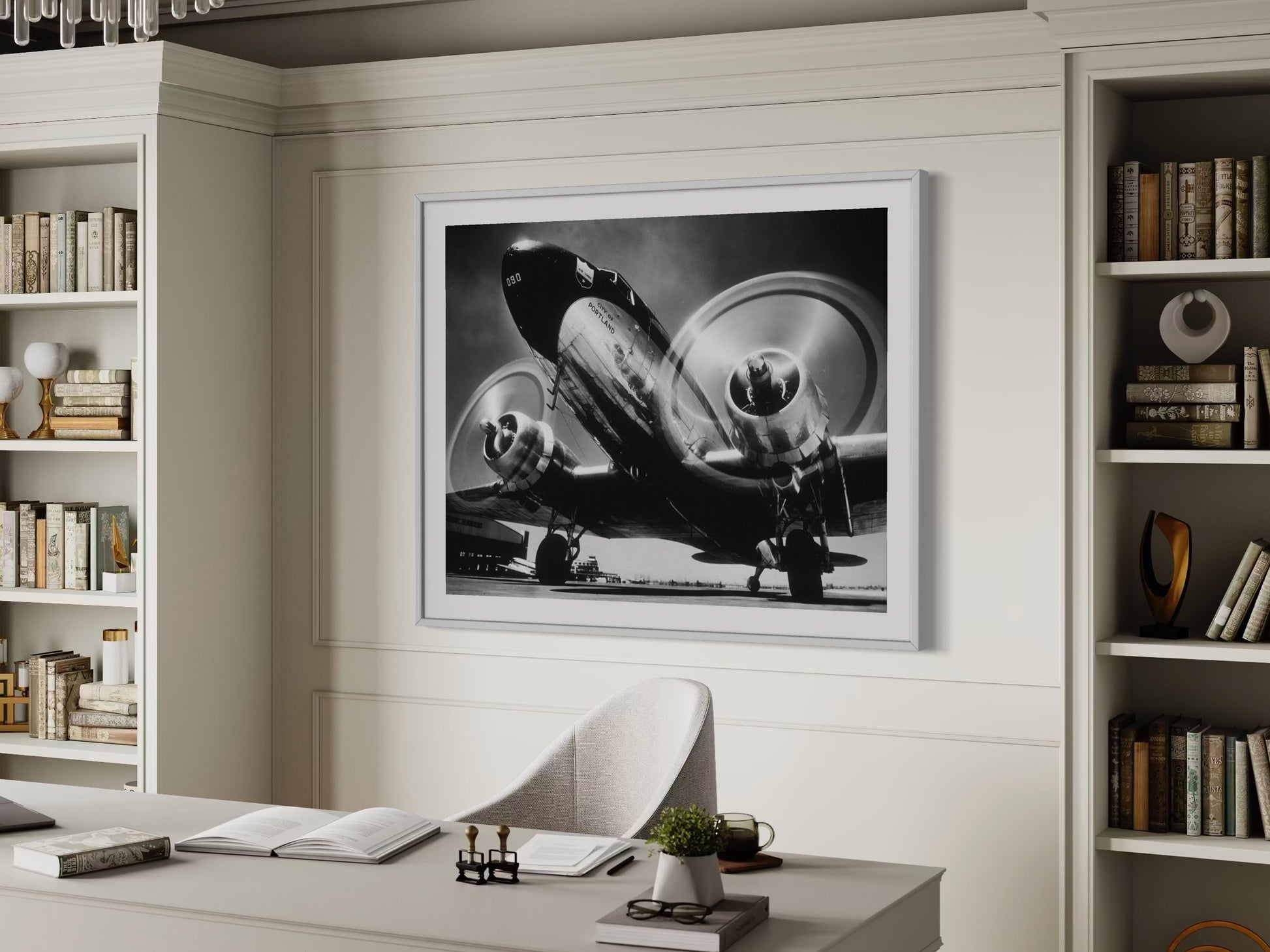 Framed black and white airplane photograph on a wall above a desk with books and decor.