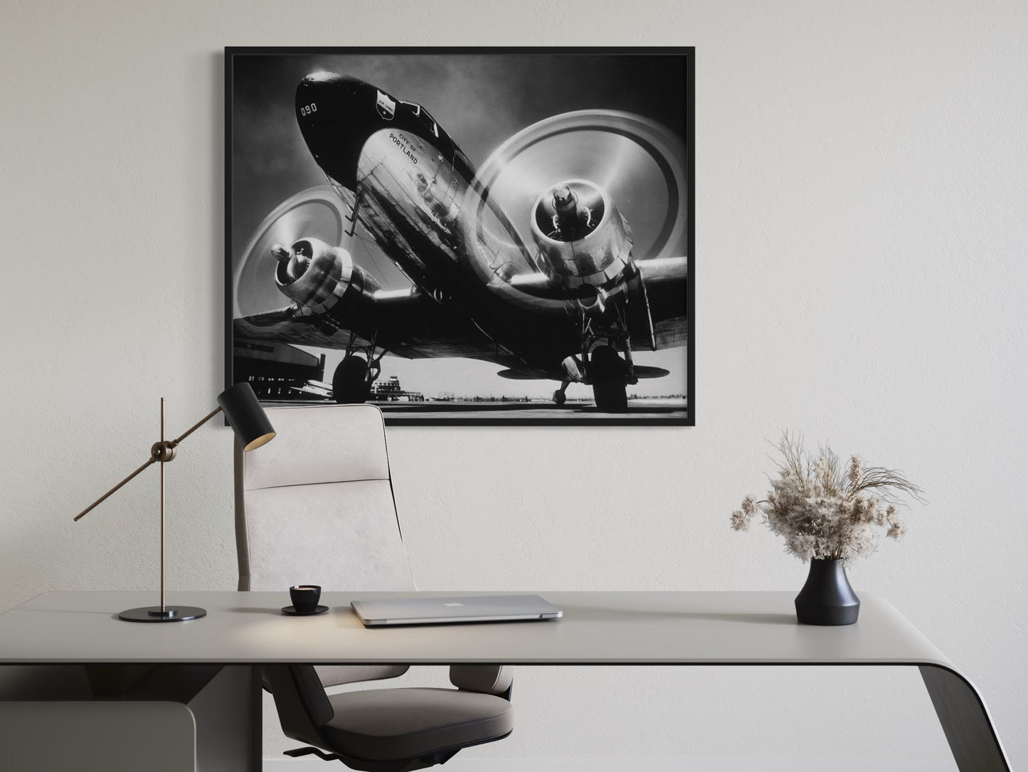 Framed black and white airplane photograph on a wall above a desk.