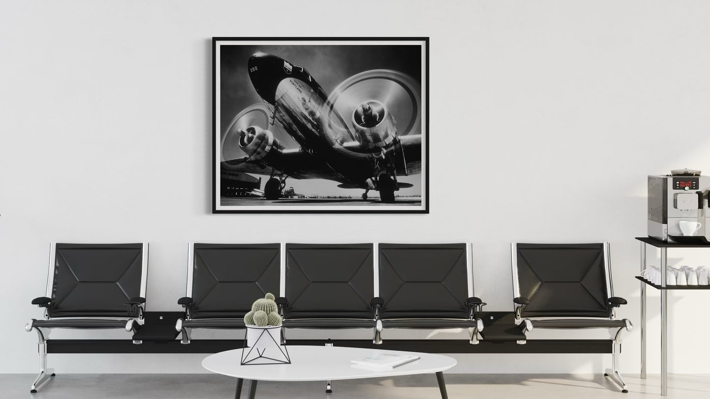 Black and white airplane photograph on a wall above a row of black chairs in a waiting room.