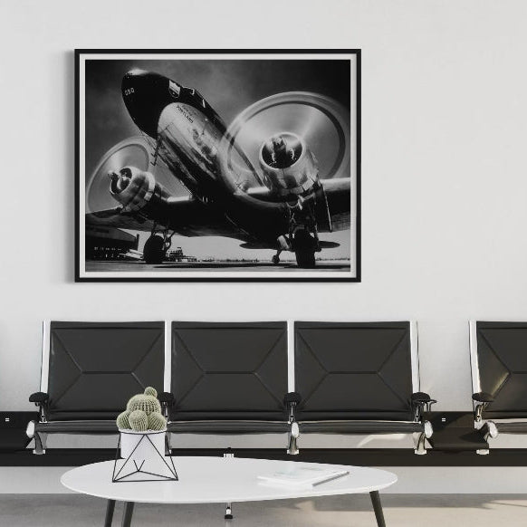 Black and white airplane photograph on a wall above a row of black chairs in a waiting room.