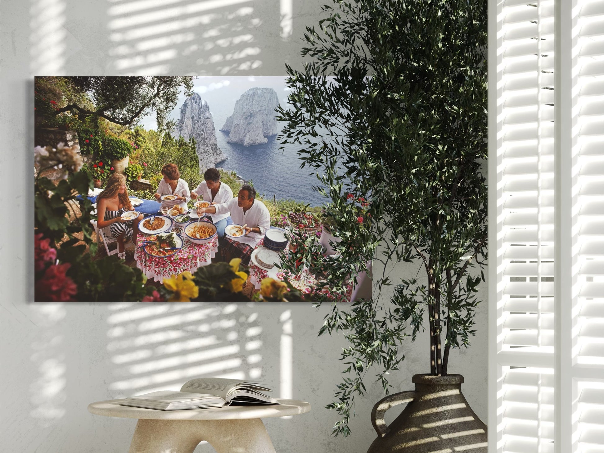 Canvas print of a group of people at a picnic with a scenic background, hanging on a wall with a plant in the foreground.