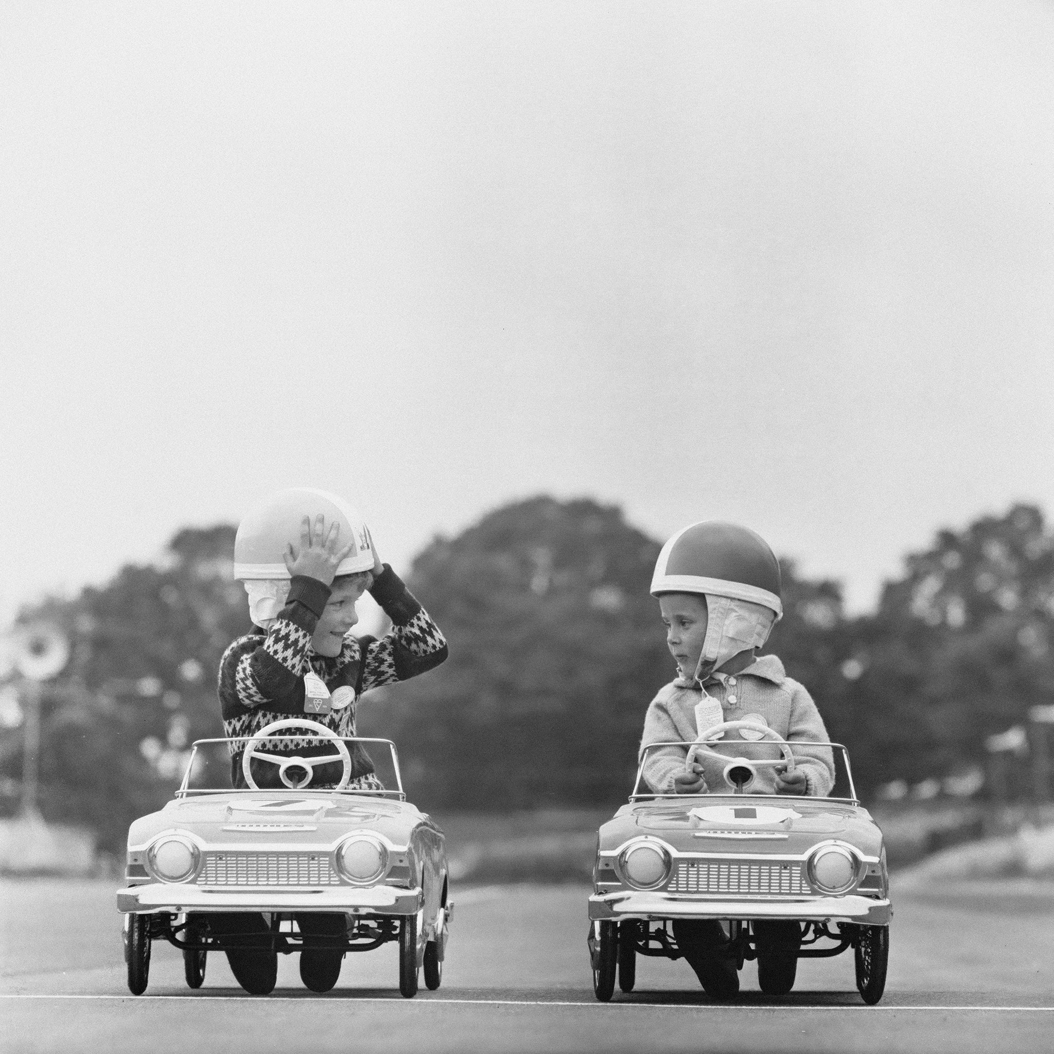 Junior Grand Prix by Express /Stringer – two children in pedal cars wearing helmets, black and white fine art photograph from Getty Images Gallery, custom framed by The Picturalist.