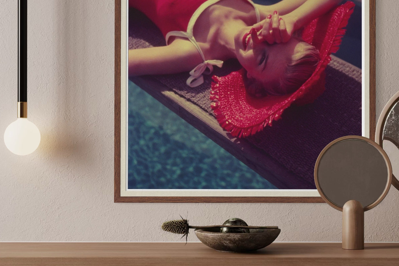 Framed artwork of a person in a red dress lying on a poolside, displayed on a wooden shelf with decorative items.