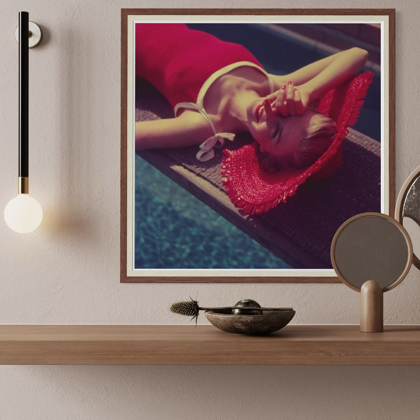 Framed artwork of a person in a red dress lying on a poolside, displayed on a wooden shelf with decorative items.