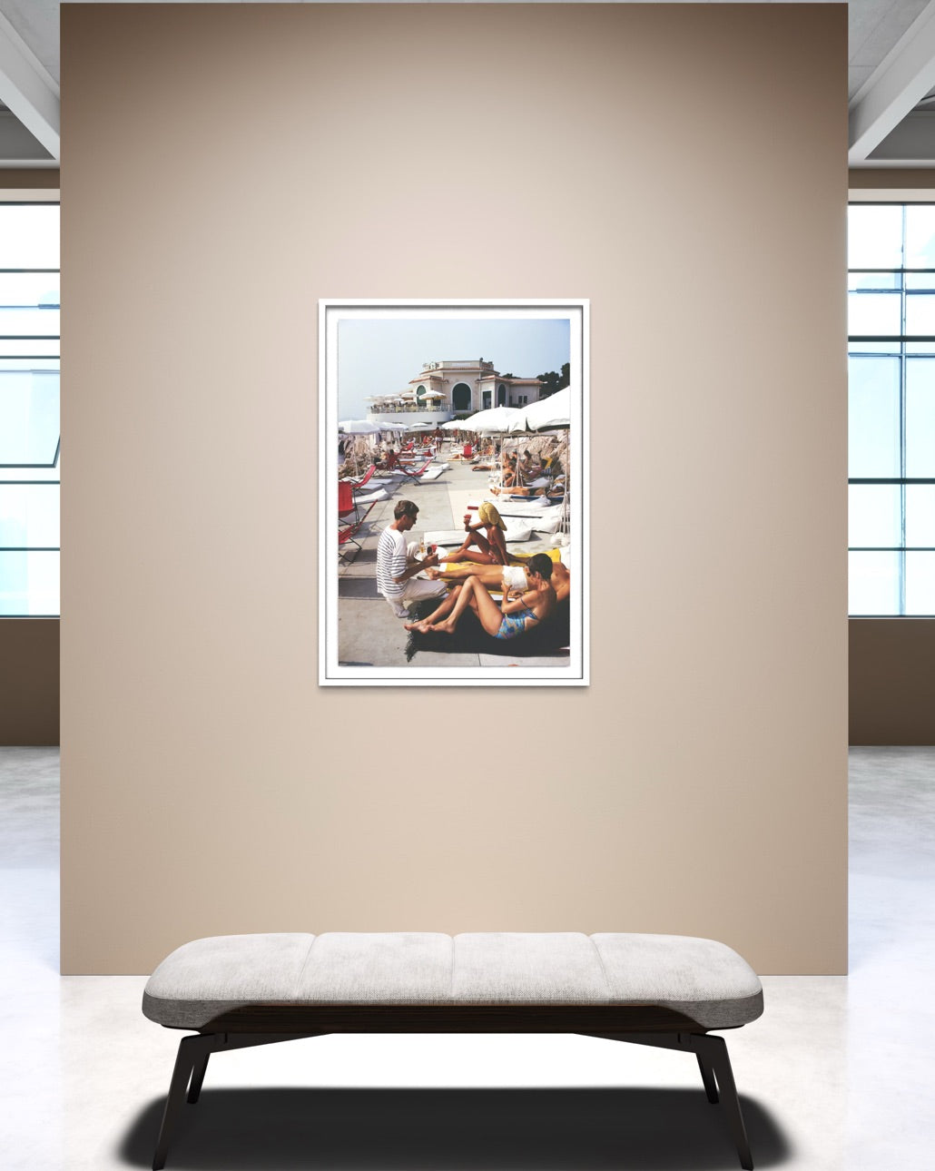 A framed art print depicting a beach scene with people is displayed on a beige wall above a modern gray bench in a minimalist room setting.
