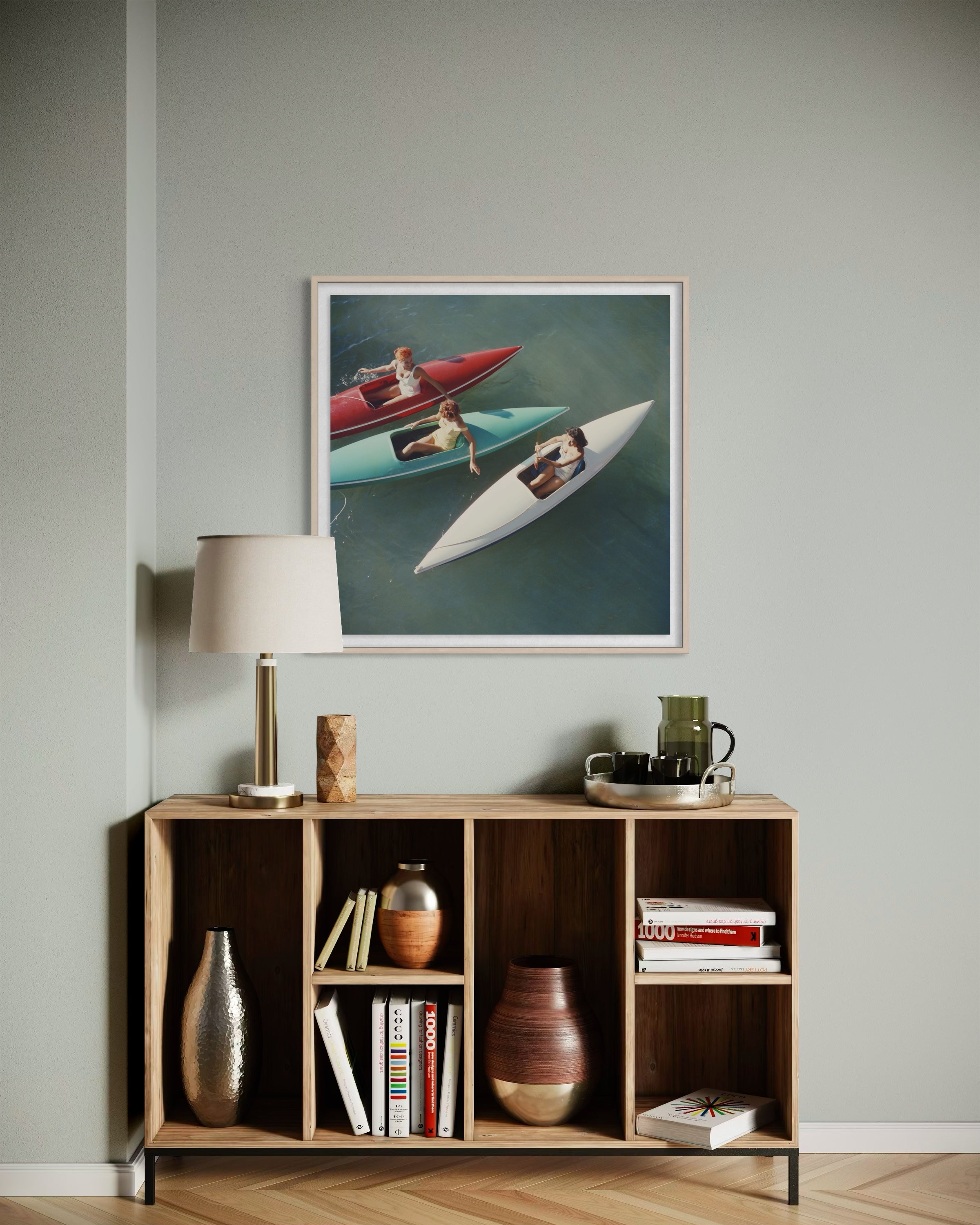 A framed art print depicting two speedboats on water, styled in a modern living room setting above a wooden bookshelf with a lamp and decorative items.