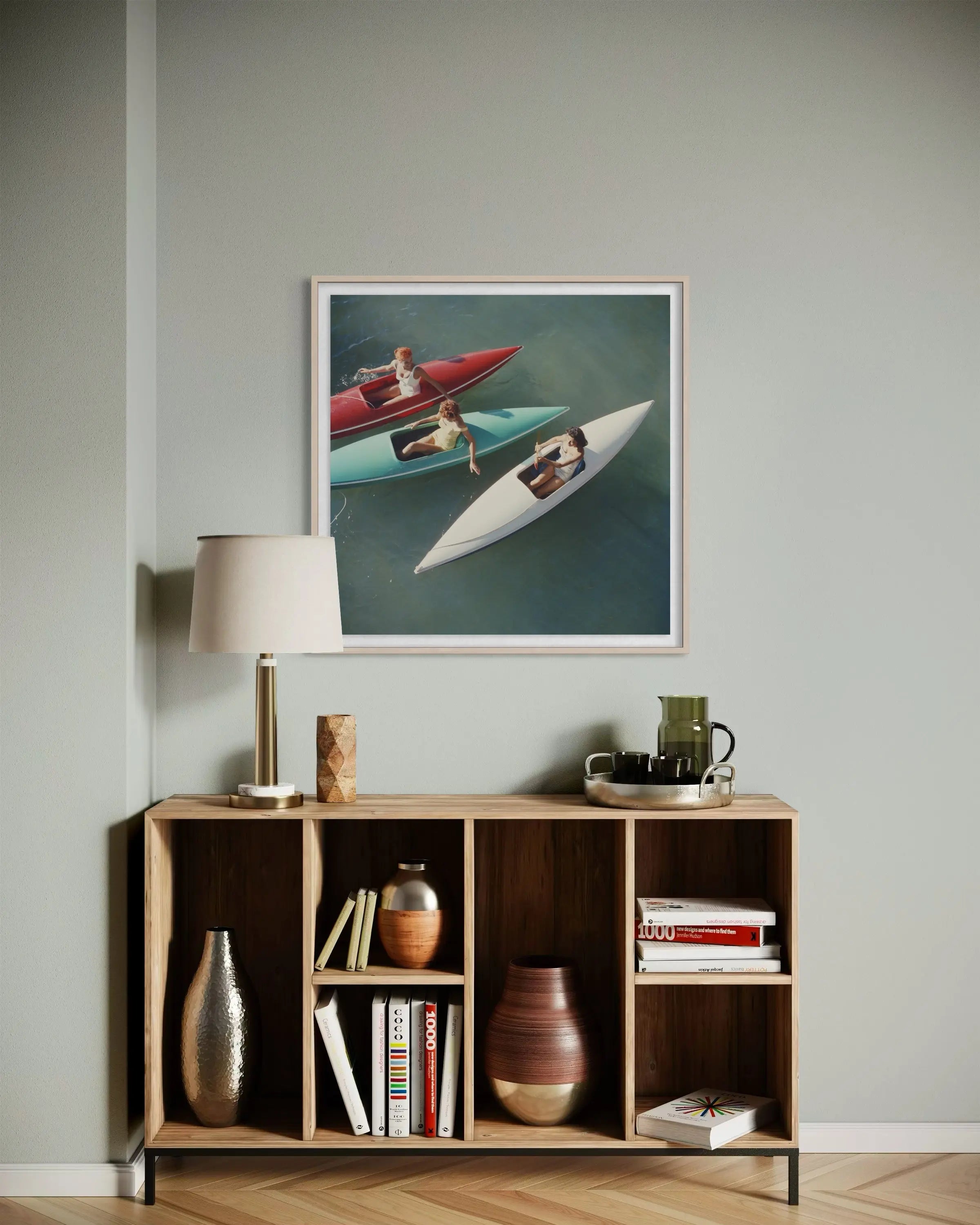 A framed art print depicting two speedboats on water, styled in a modern living room setting above a wooden bookshelf with a lamp and decorative items.