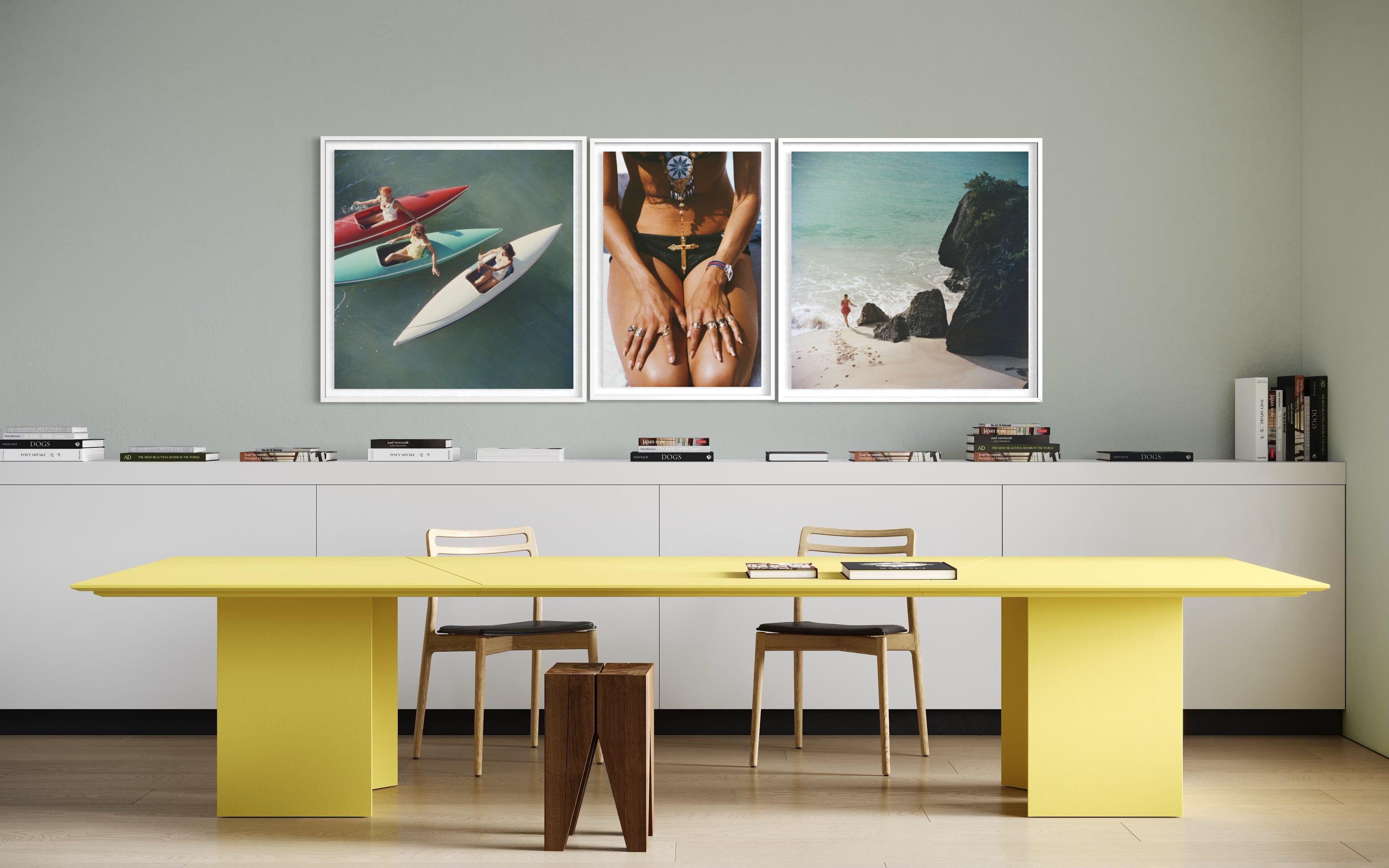 A modern interior scene with a bright yellow table and chairs in front of a white cabinet, above three framed art prints on a light gray wall.