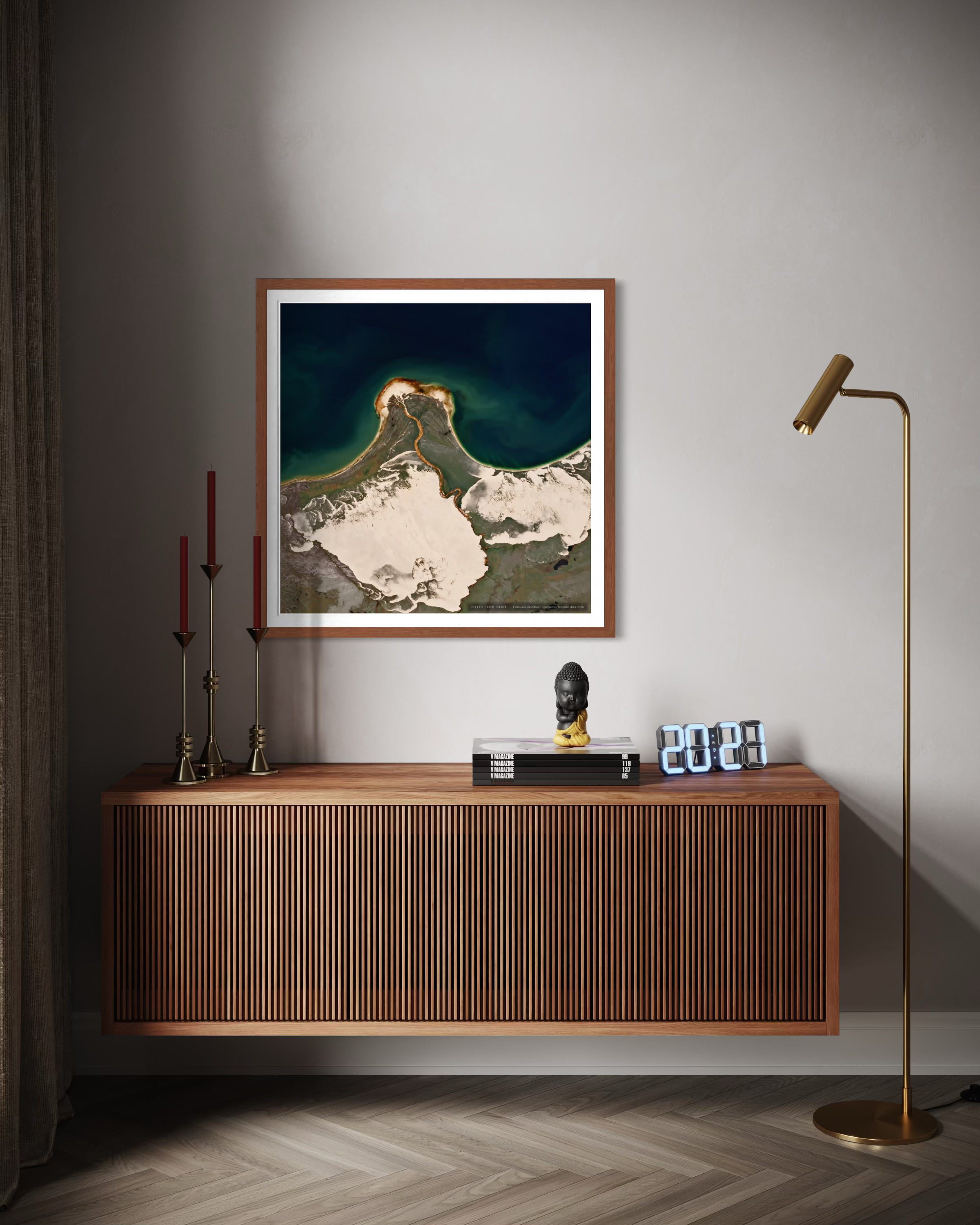 A framed art print depicting a mountain landscape with snow and dark teal sky, styled on a gray wall above a wooden console table in a modern room setting.