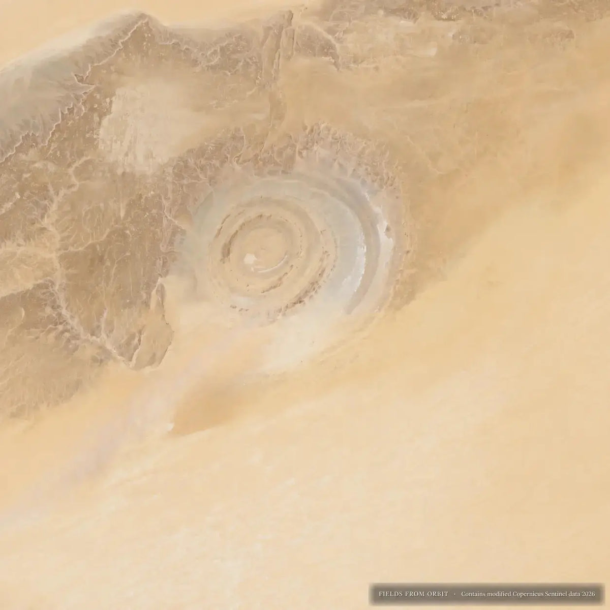 Aerial satellite photograph of a circular salt flat or desert formation surrounded by sandy terrain, with pale beige and tan tones throughout.