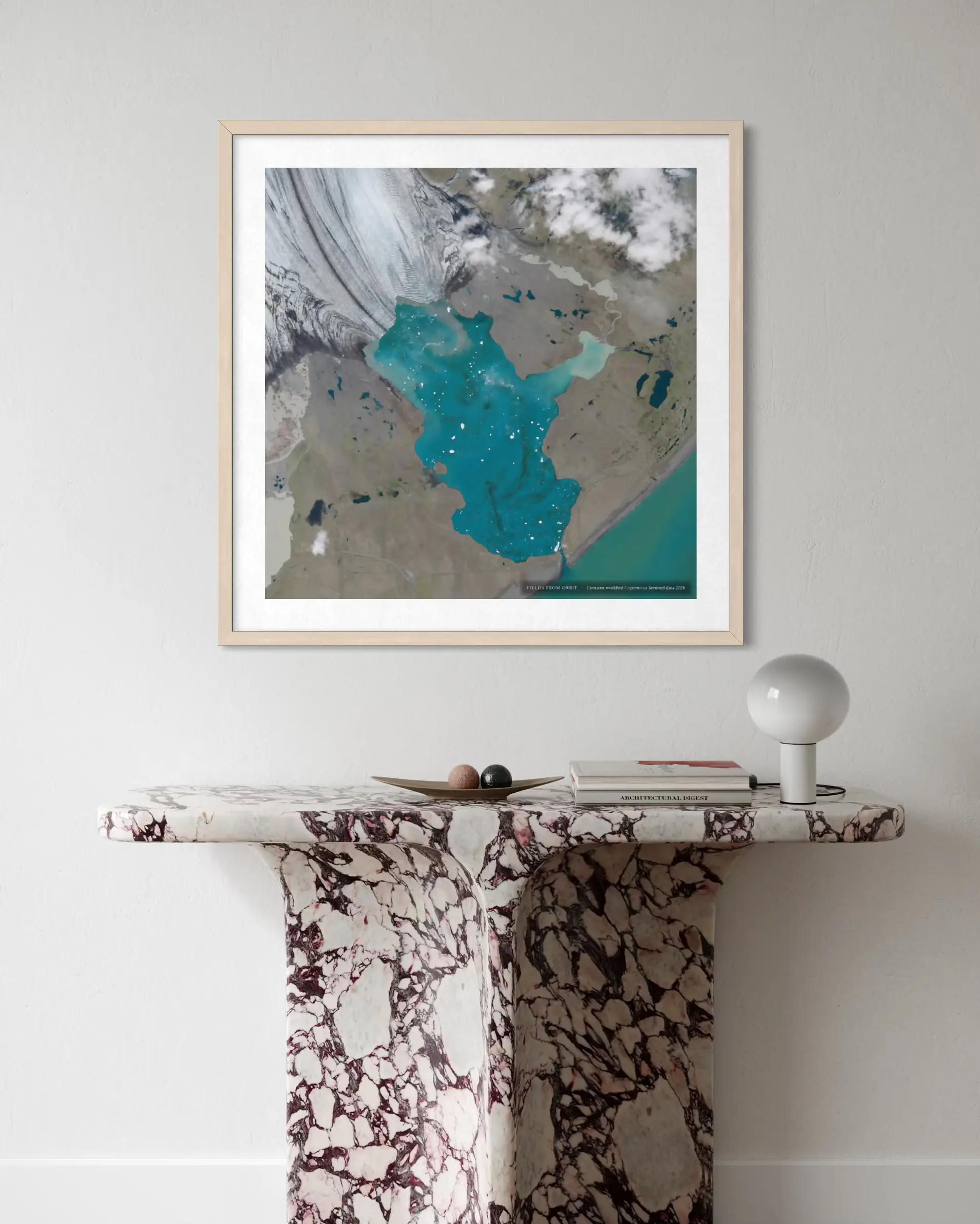 A framed art print featuring a modern abstract map of Iran in teal, gray, and white, styled on a light gray wall above a marble console table with a white lamp.