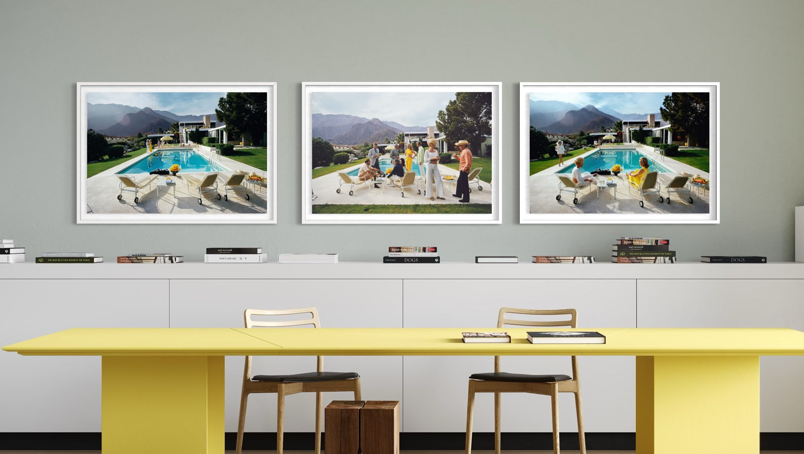 A set of three framed art prints depicting outdoor poolside scenes, displayed on a gray wall above a modern yellow table and white chairs.