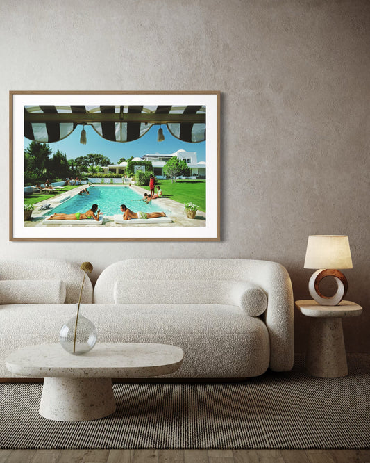 Framed artwork of a pool scene on a wall above a sofa in a living room.