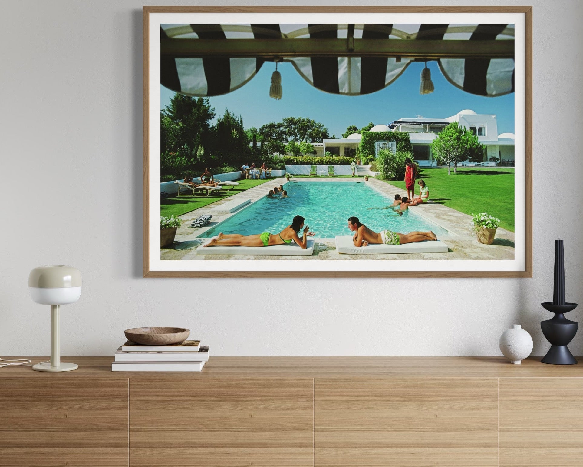 Framed artwork of a pool scene on a wall above a wooden cabinet.