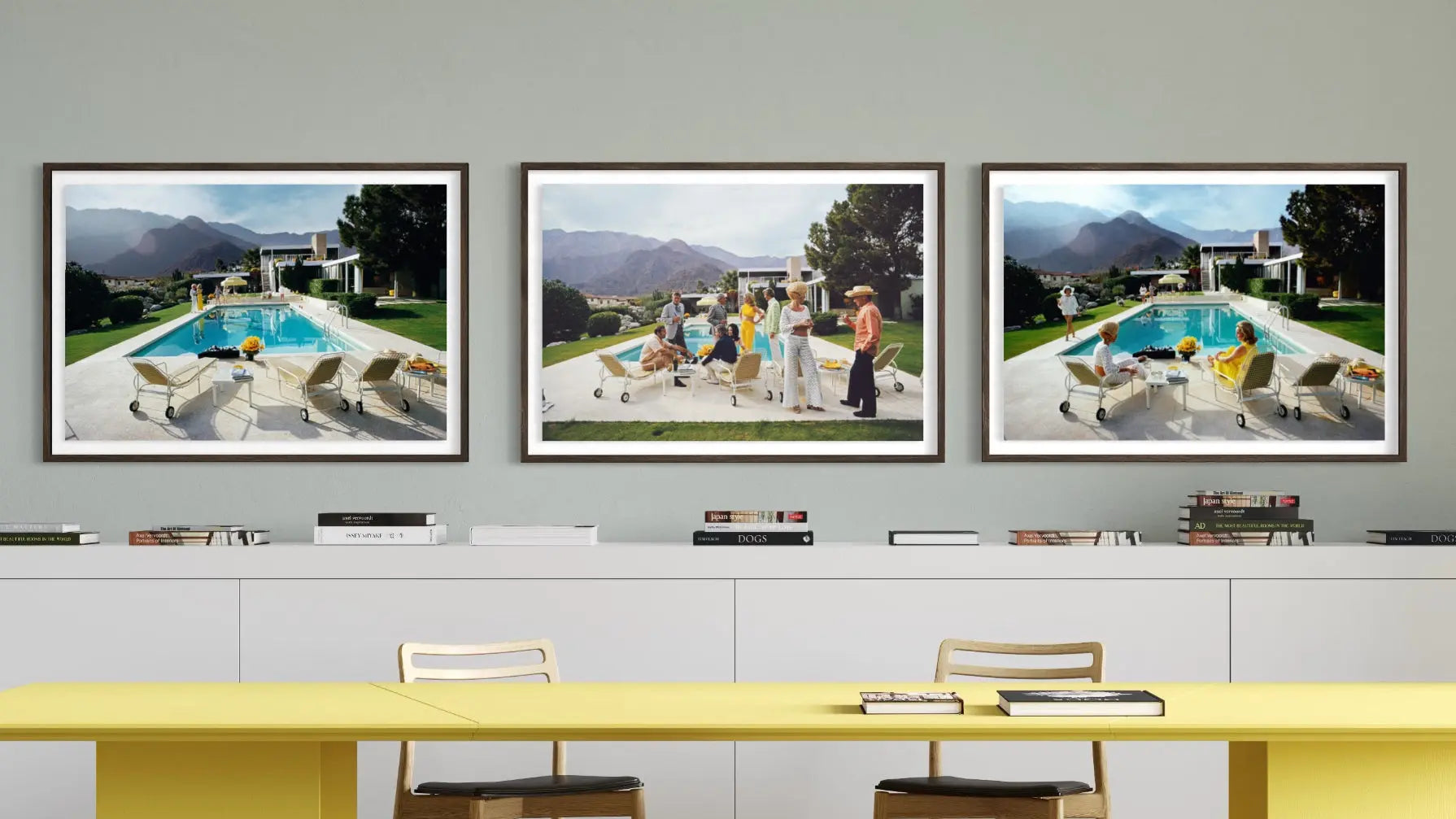 A set of three framed art prints depicting poolside scenes with people, displayed on a gray wall above a white cabinet and a yellow table. The Picturalist Wall Art and Photography for Designed Interiors. Slim Aarons Collection, Poolside. Getty Images Gallery.