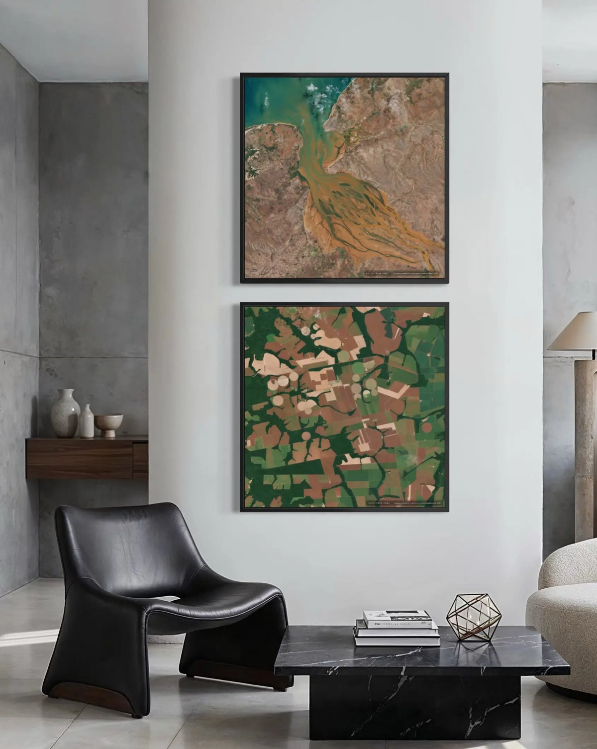 Two framed abstract landscape art prints are displayed vertically on a white wall in a modern living room setting. The top print features a golden-brown bird over green and brown terrain, and the bottom print shows a patchwork of green, brown, and beige fields.