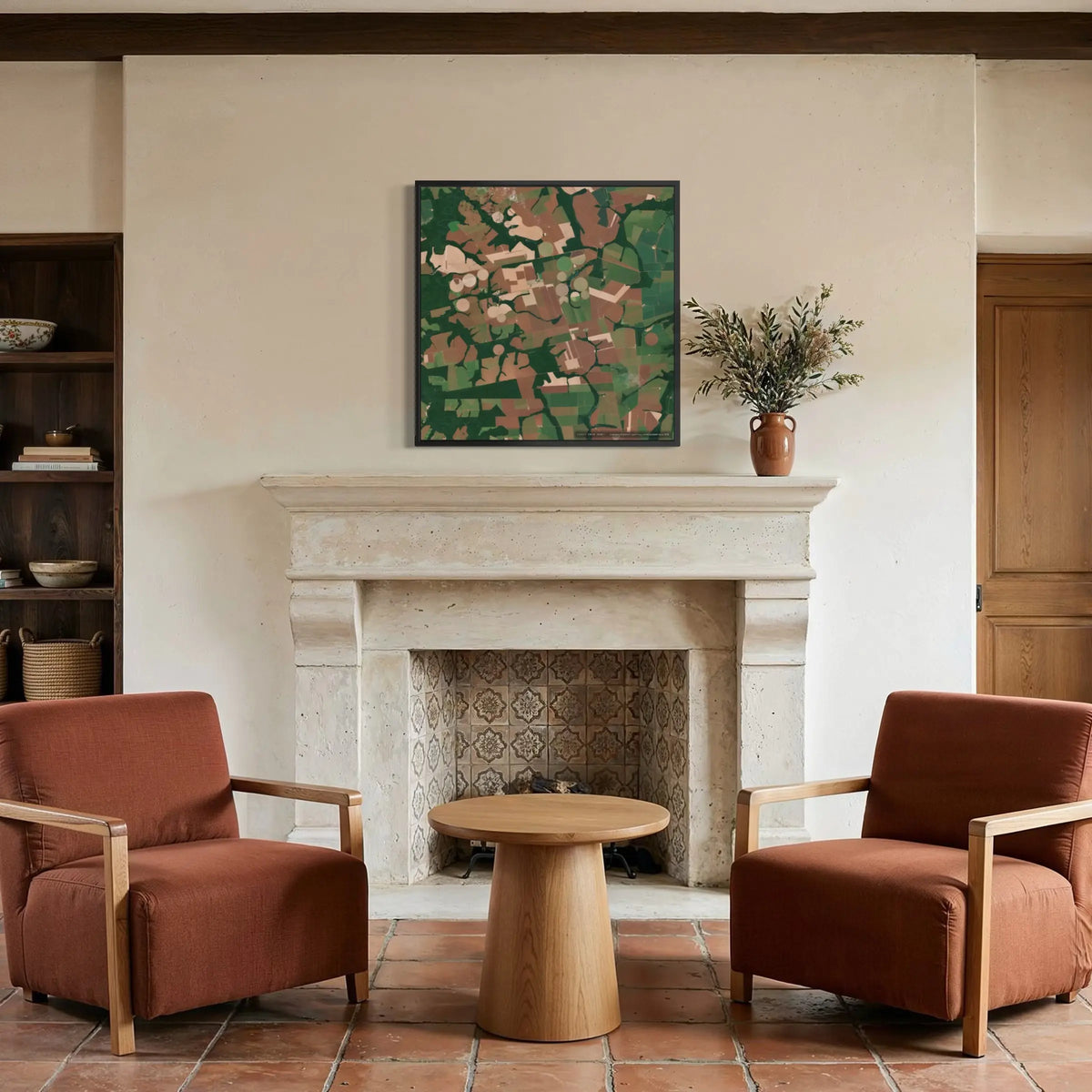 An abstract landscape painting in green, brown, and beige tones hangs on a cream wall above a stone fireplace in a rustic living room setting with two rust-colored armchairs and a wooden side table.