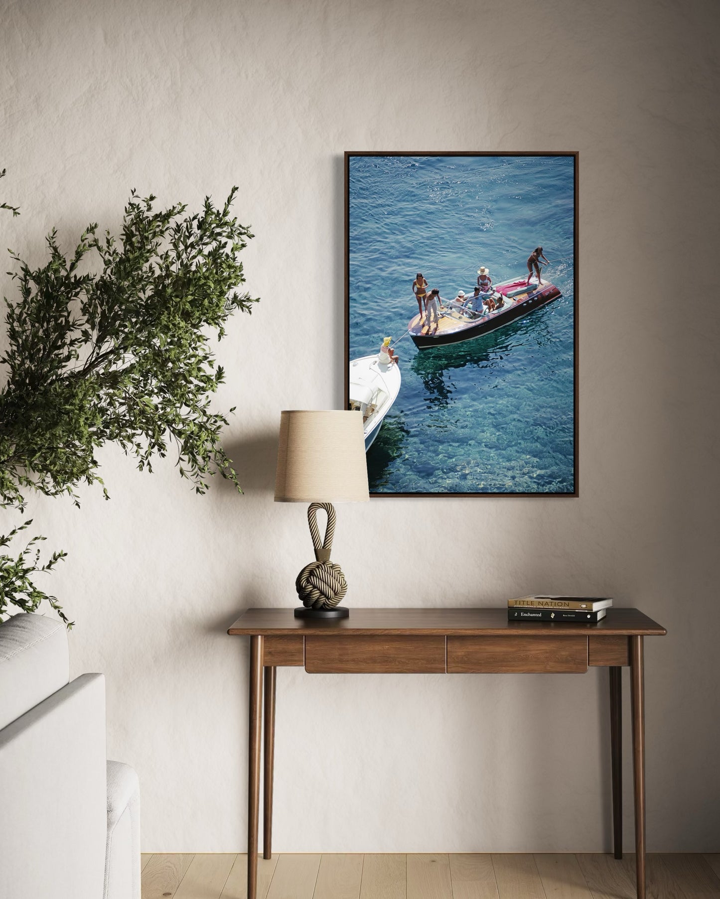 Framed artwork of people on a boat hanging above a wooden console table with a lamp.